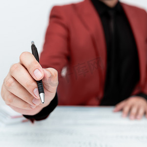 穿着红色西装的男模特坐在白桌旁，用笔指着重要信息。