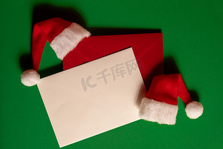 圣诞节绿色帽子摄影照片_绿色背景上有空纸卡便条信封的圣诞老人帽子。