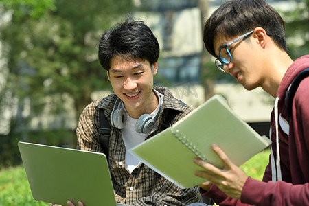 一群大学生讨论他们的家庭作业，在校园的绿草上使用笔记本电脑。