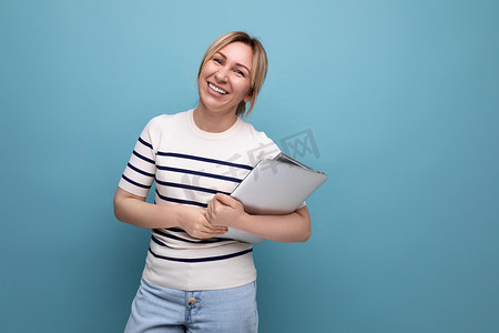 条纹毛衣摄影照片_一位成功的金发女性自由职业者的特写，她身穿条纹毛衣，手里拿着蓝色背景的笔记本电脑
