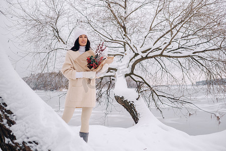 一个穿着米色开衫和冬花的女孩在下雪的季节在大自然中漫步。