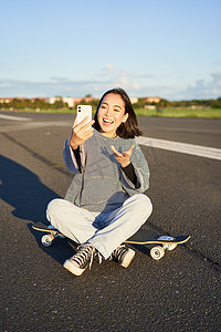 积极的亚洲少女自拍，在手机应用上视频聊天，坐在滑板上录制视频博客