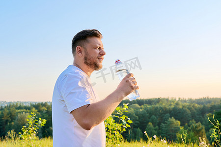 在阳光明媚的炎热夏日，留着胡须的中年男子从瓶子里喝水。