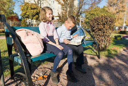 小男孩和女孩小学生读书，坐在长凳上，背着背包的孩子