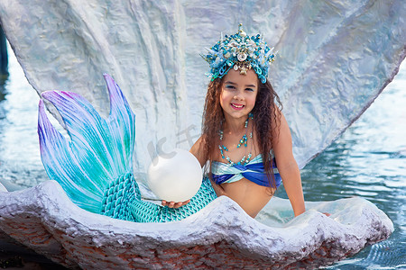 一个穿着美人鱼服装的美丽快乐的小女孩坐在一个大海壳里