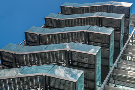 应急出口摄影照片_具有重复结构和反射天空和云彩的现代办公楼中带金属应急梯/防火梯的商务大楼。