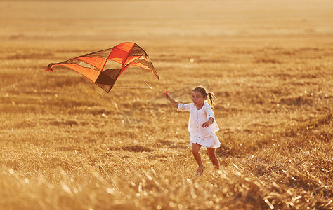 风筝玩具摄影照片_夏天，快乐的小女孩在田野里带着红风筝在户外奔跑