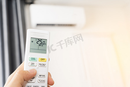 人手正在使用空调的白色遥控器打开或调节室内空调的温度。