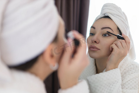一位女士用化妆刷在睫毛上涂抹黑色睫毛膏。