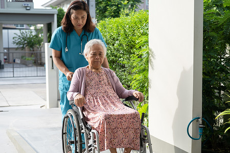 老女性摄影照片_看护者帮助和照顾坐在轮椅上的护理医院坡道上的亚洲老年或老年老妇人患者，健康强大的医疗理念