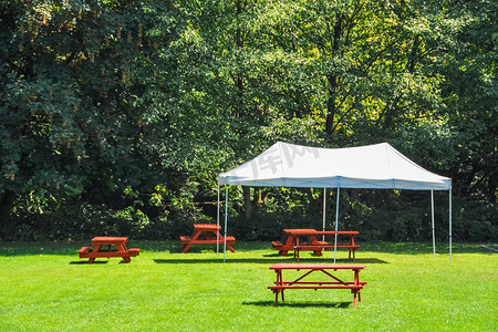 公园绿色草坪上带红色野餐桌和白色帐篷的休息区