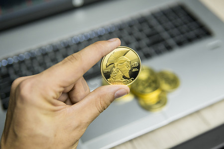 男性商人手拿着树泰坦比特币在笔记本电脑键盘和一堆金币的背景上。
