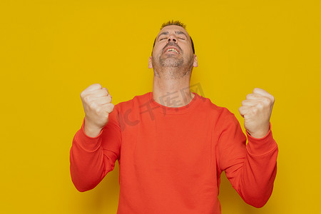 一个心满意足的男人举起拳头庆祝成功并在黄色背景中孤立地抬头的肖像