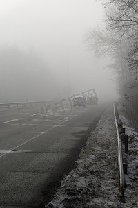 行驶着的汽车摄影照片_汽车在雾蒙蒙的路上行驶，车头灯或前灯亮着。