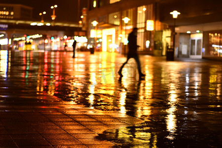 雨晚上摄影照片_在德国埃森的车站前院，男子在雨中黑暗中行走