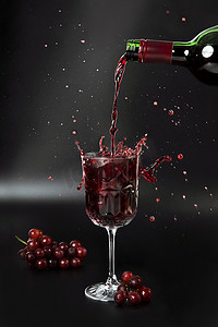 红酒被倒入黑色背景的酒杯中，上面有葡萄和飞溅