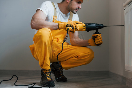 身穿黄色制服的杂工在室内使用电钻。