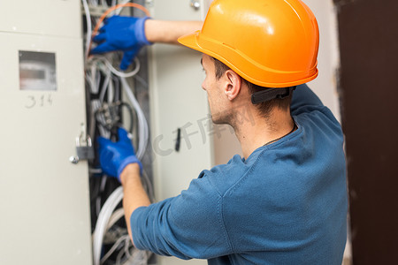 老年电工修理工在统一工作、固定、在保险丝盒中安装以太网电缆、手持手电筒和电缆的特写镜头。