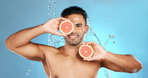 在蓝色工作室背景下，男人、肖像微笑和水果用于护肤、健康营养或维生素 C 和水合作用。