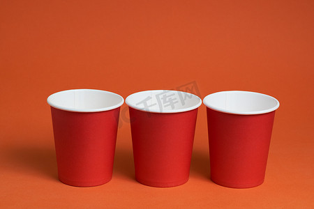 红色茶摄影照片_棕色背景上的三个红色一次性杯子。