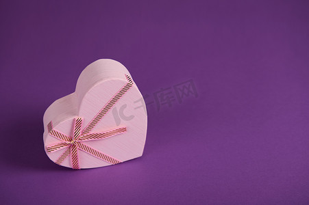 可爱的粉红色心形礼品盒，里面有浪漫的惊喜，在明亮的紫色背景中被隔离。