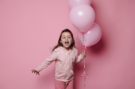 粉红色背景中的孤立肖像，是生日快乐的女孩，她摆着一束粉色柔和的氦气气球