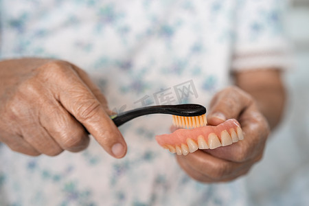 亚洲老年妇女患者使用牙刷清洁替换牙齿的局部义齿。