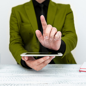 身穿绿色夹克的商人坐在桌旁，拿着手机，用一根手指指着重要信息。
