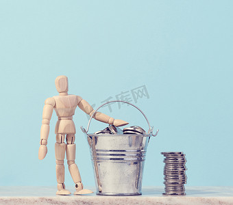 蓝色背景中微型桶中的木制人体模型和硬币，高收入、补贴的概念