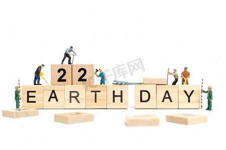 人物海报设计背景摄影照片_微型人物：工人团队在木制背景的木块上建造“地球日”字样，地球日概念