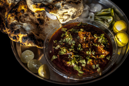 阿凡提卡通摄影照片_Achari Chicken 和 tandoori roti 一起放在盘子里，还有一些辣椒、洋葱和柠檬。
