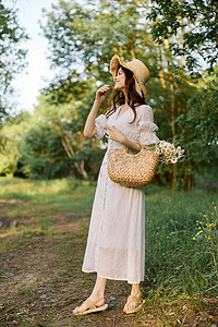 一位身穿浅色夏装、头戴柳条帽的女士站在森林里，手里拿着一篮雏菊