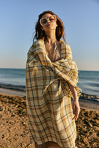 花纹红摄影照片_日落时分，一个可爱的女人穿着格子呢站在沙滩上，风吹动着她的红头发。