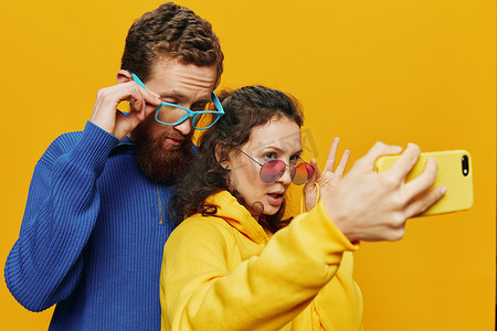 生活搞笑摄影照片_在黄色背景下，女人和男人带着手机的搞笑情侣手握社交网络和歪歪扭扭的交流自拍微笑很有趣。