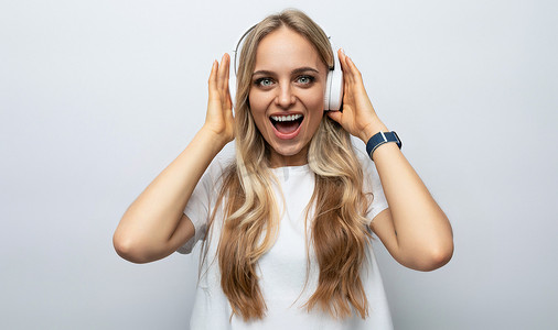 戴着白色耳机的情绪化年轻女性在白色工作室背景下收听播客