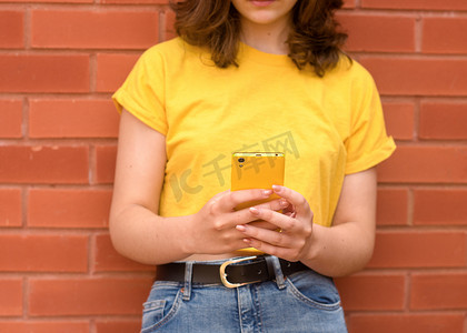 身穿黄色衬衫的年轻女子靠着砖墙打电话聊天