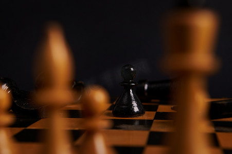 专注于黑色木棋子，一只爪子在白色棋子模糊的前景上移动，黑色背景中突显