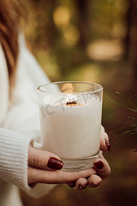 秋天森林里一个女孩在户外拿着燃烧的蜡烛的手的特写镜头