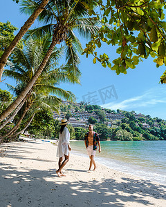 泰国普吉岛，一对男女在棕榈树环绕的白色热带海滩上散步