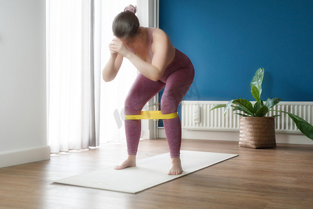 女人在家健身时腿上绑着橡胶阻力带做深蹲