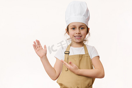 穿着厨师制服的迷人小女孩，对着镜头甜甜地微笑，把手指着一个空白的地方做广告文字