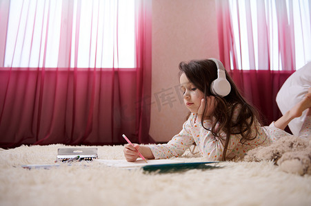 穿着睡衣的可爱小女孩，用无线耳机听音乐，用彩色铅笔画画