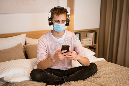 戴耳机躺在床上的男人戴着防护面罩，手里拿着电话