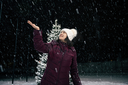 城市下雪摄影照片_在一个下雪的夜晚，一个愉快的女人在城市街道上行走时，手上抓着雪花。