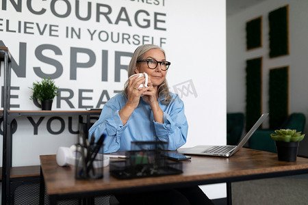 坐着的会计摄影照片_成年坚强独立的女人坐在办公室里，手里拿着一杯茶。
