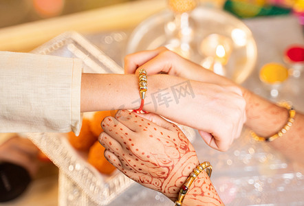 手部特写，姐妹在节日或仪式上将 rakhi、Raksha bandhan 绑在兄弟的手腕上 — Rakshabandhan 在印度各地庆祝为无私的爱或兄弟姐妹之间的关系