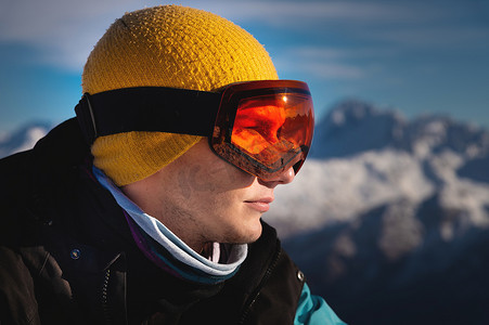 阳光明媚的日子里，男性滑雪者俯瞰积雪覆盖的山脉，滑雪护目镜反射阳光