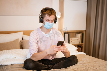 戴耳机躺在床上的男人戴着防护面罩，手里拿着电话