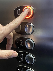 电梯按钮摄影照片_手指按下带灯的电梯按钮。