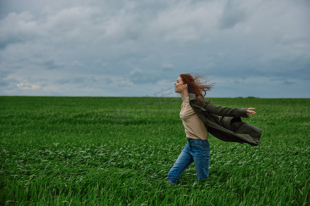 一个穿大衣的女人在多云的天气里站在田野里抵抗强风